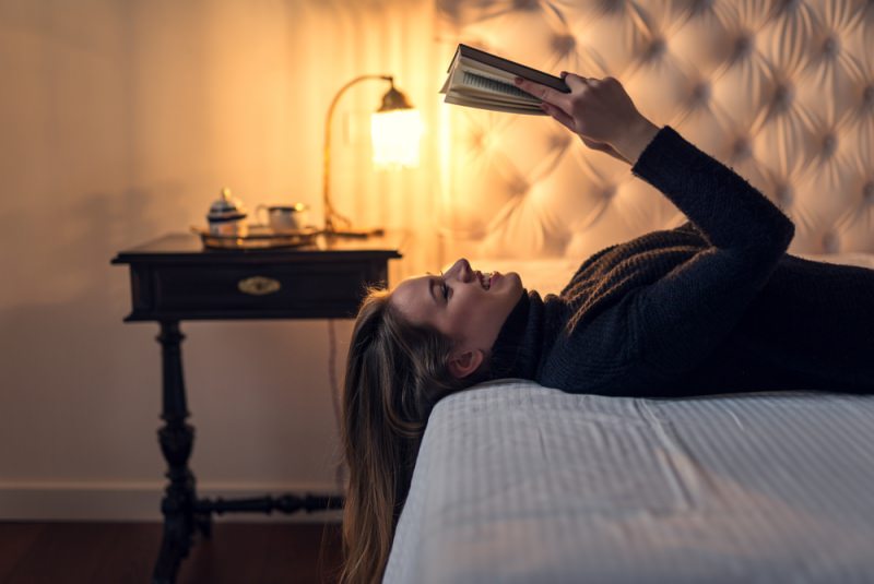 donna sorridente legge sul letto con luce calda comodino